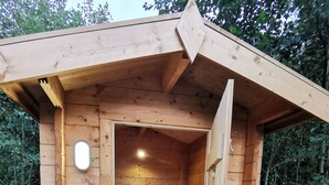 Un sauna en bois, dont la porte est ouverte, laissant apercevoir un banc à l’intérieur.
