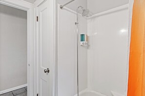Un baño con puerta blanca, ducha con cabezal de ducha de mano y dispensador de jabón en la pared.