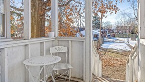 A covered porch with a white table and chair, a tree, and a view of a snowy yard.
