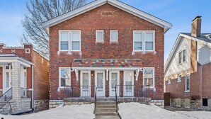 A two-story brick building with a central entrance, numbered doors, and a small porch with railings.