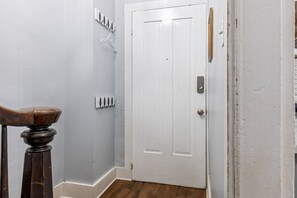 A hallway with a white door, a coat rack, and a wooden chair. - Historic 1805 Main Street 2BR (Saint Charles)