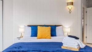 A neatly made bed with blue and white bedding, a yellow accent pillow, and a stack of white towels on a wooden tray. - Historic 1805 Main Street 2BR (Saint Charles)