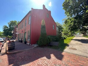 Un bâtiment en briques rouges surmonté d’un jardin ornemental vert, avec un banc et une rue pavée.