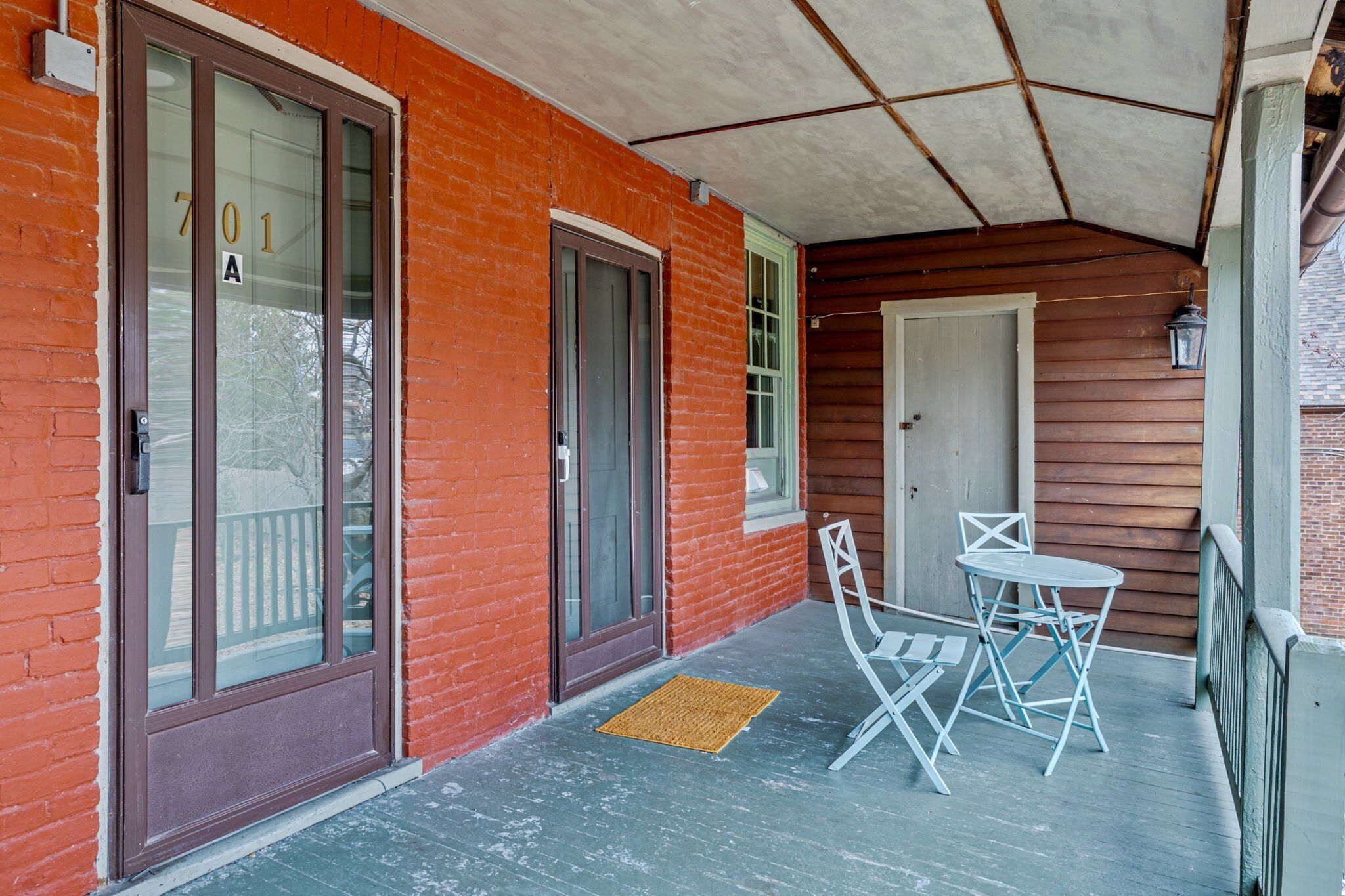 A covered porch with a brick exterior, a door labeled "701 A", and a small table with chairs.