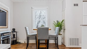 A dining area with a wooden table and four grey upholstered chairs. There is a potted plant on the right side. - Historic 1805 Main Street 2BR (Saint Charles)