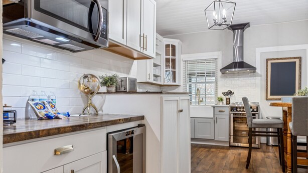 A modern kitchen with white cabinetry, stainless steel appliances, and a dining area with a wooden table and chairs. - Historic 1805 Main Street 2BR (Saint Charles)