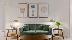 A modern living room with a green sofa, two side tables, and three framed artworks on the wall. - Historic 1805 Main Street 2BR (Saint Charles)