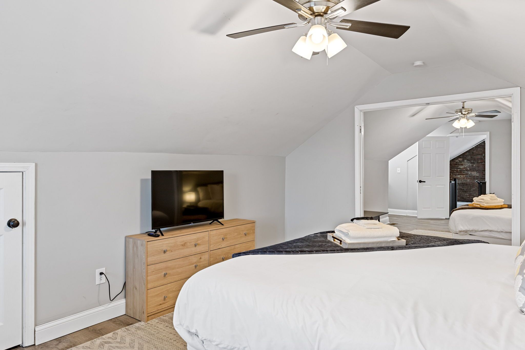 A modern bedroom with a large bed, a TV on a wooden dresser, and a ceiling fan.