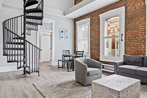 Un salon moderne avec un escalier en colimaçon, un mur en briques, un coin repas et un canapé gris.