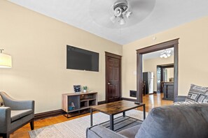 A living room with a flat-screen TV, a wooden coffee table, a grey sofa, and a ceiling fan.