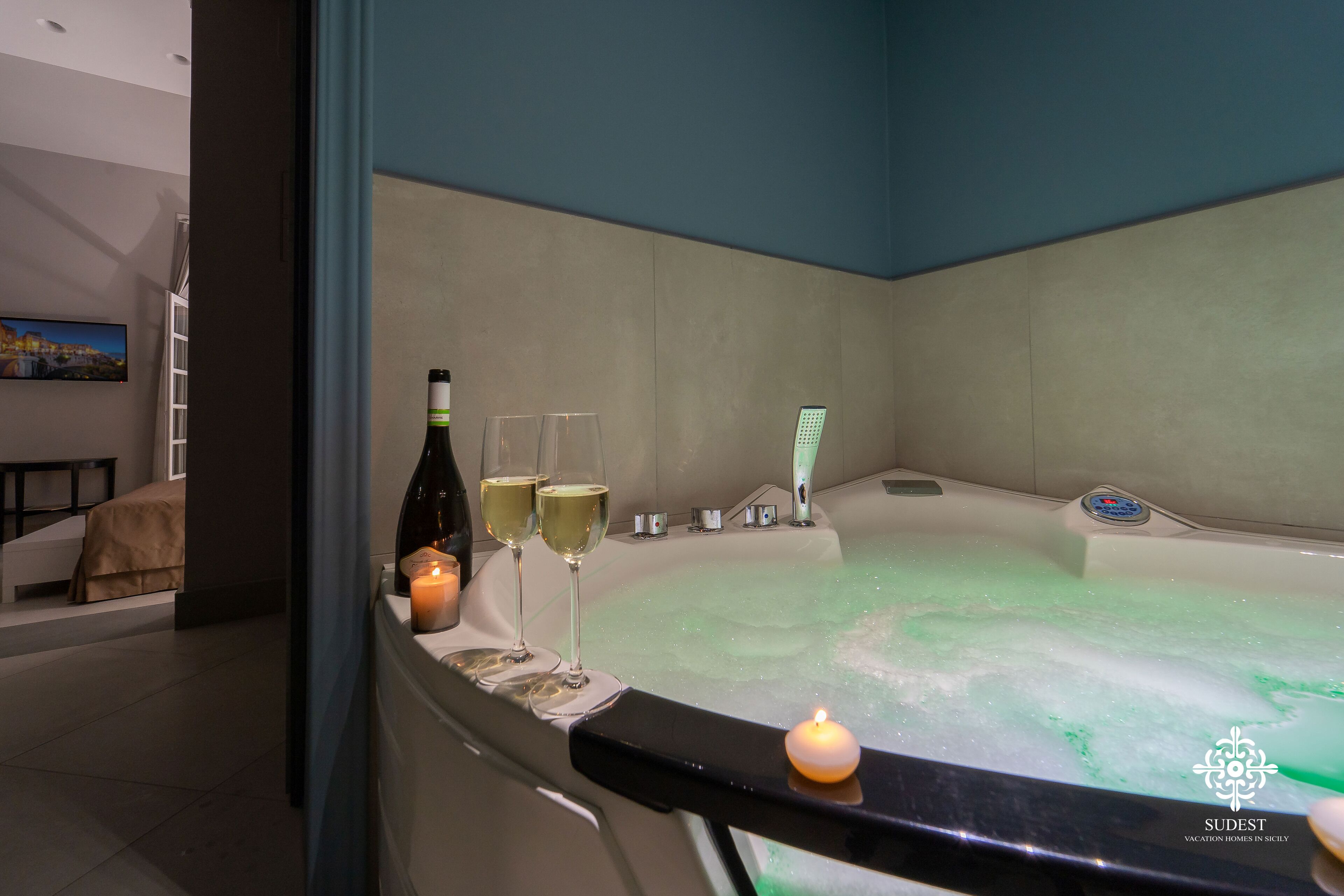 A spa room with a hot tub, two glasses of wine, and a candle on the edge.