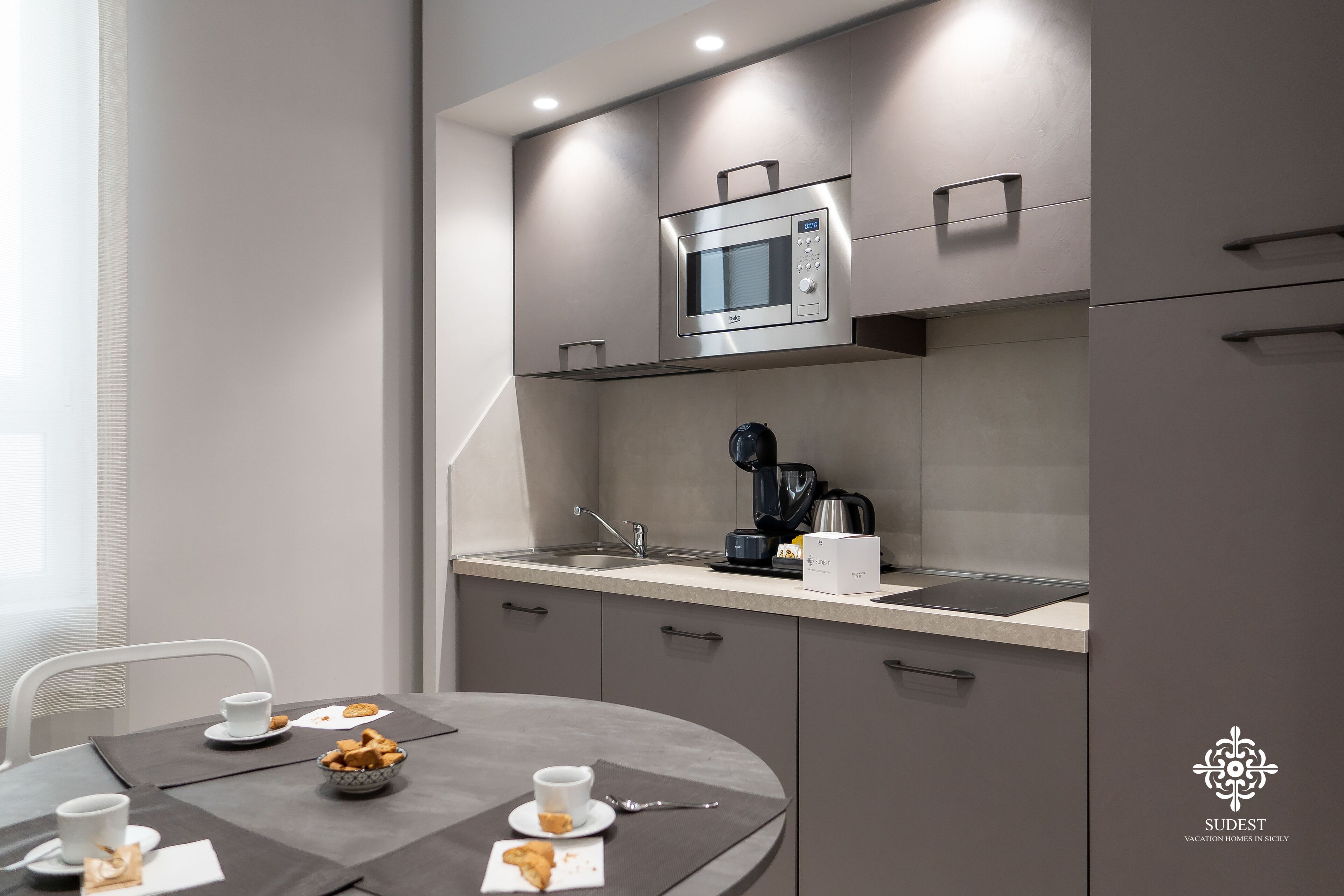 A modern kitchen with a microwave, coffee maker, and a sink. There is a dining table with a few items on it.