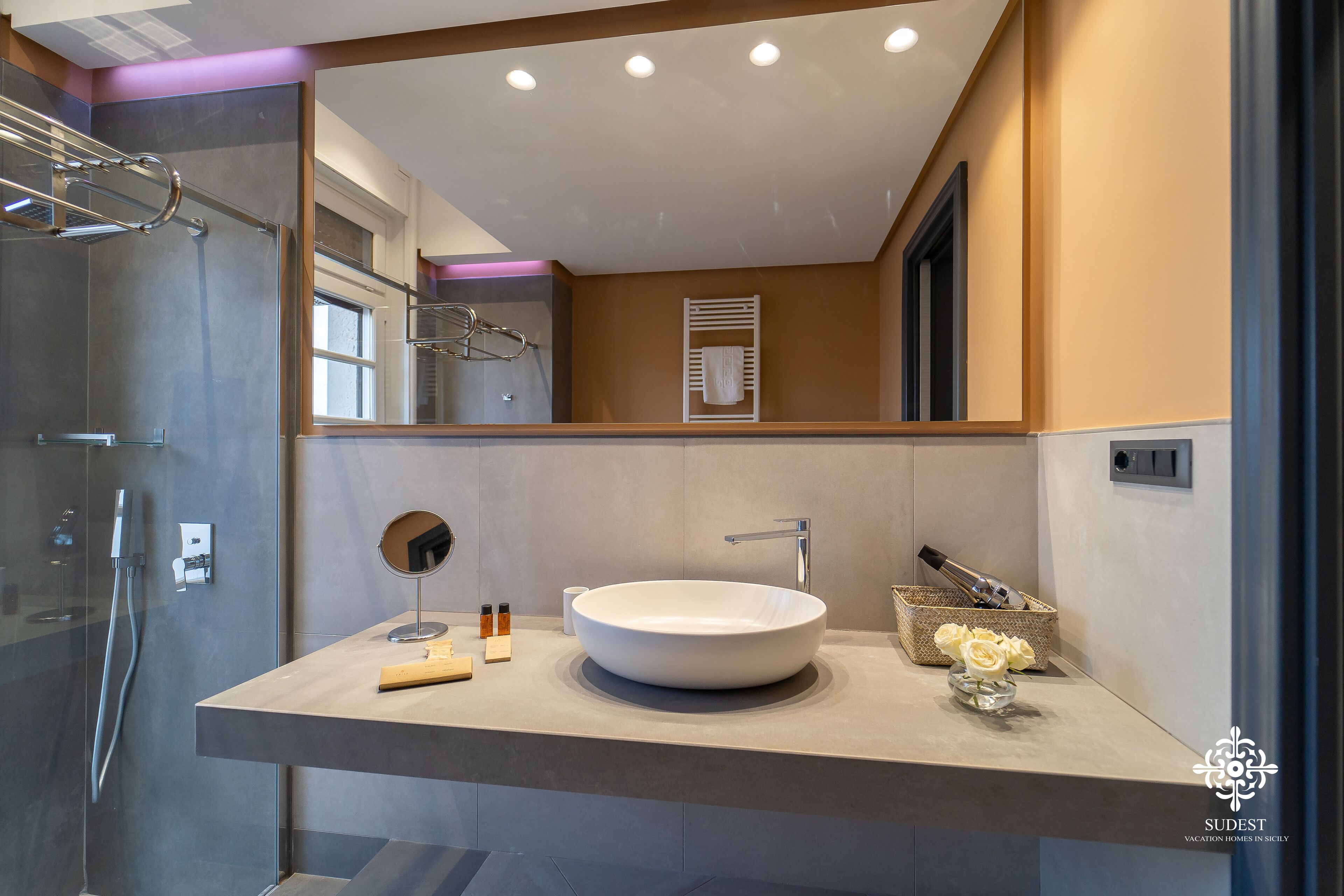 A modern bathroom with a large mirror, a round sink, and a glass shower enclosure.