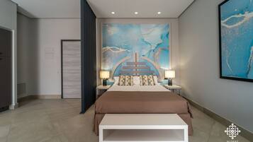 A modern bedroom with a large bed, two bedside tables with lamps, a large abstract painting on the wall, and a bench at the foot of the bed.