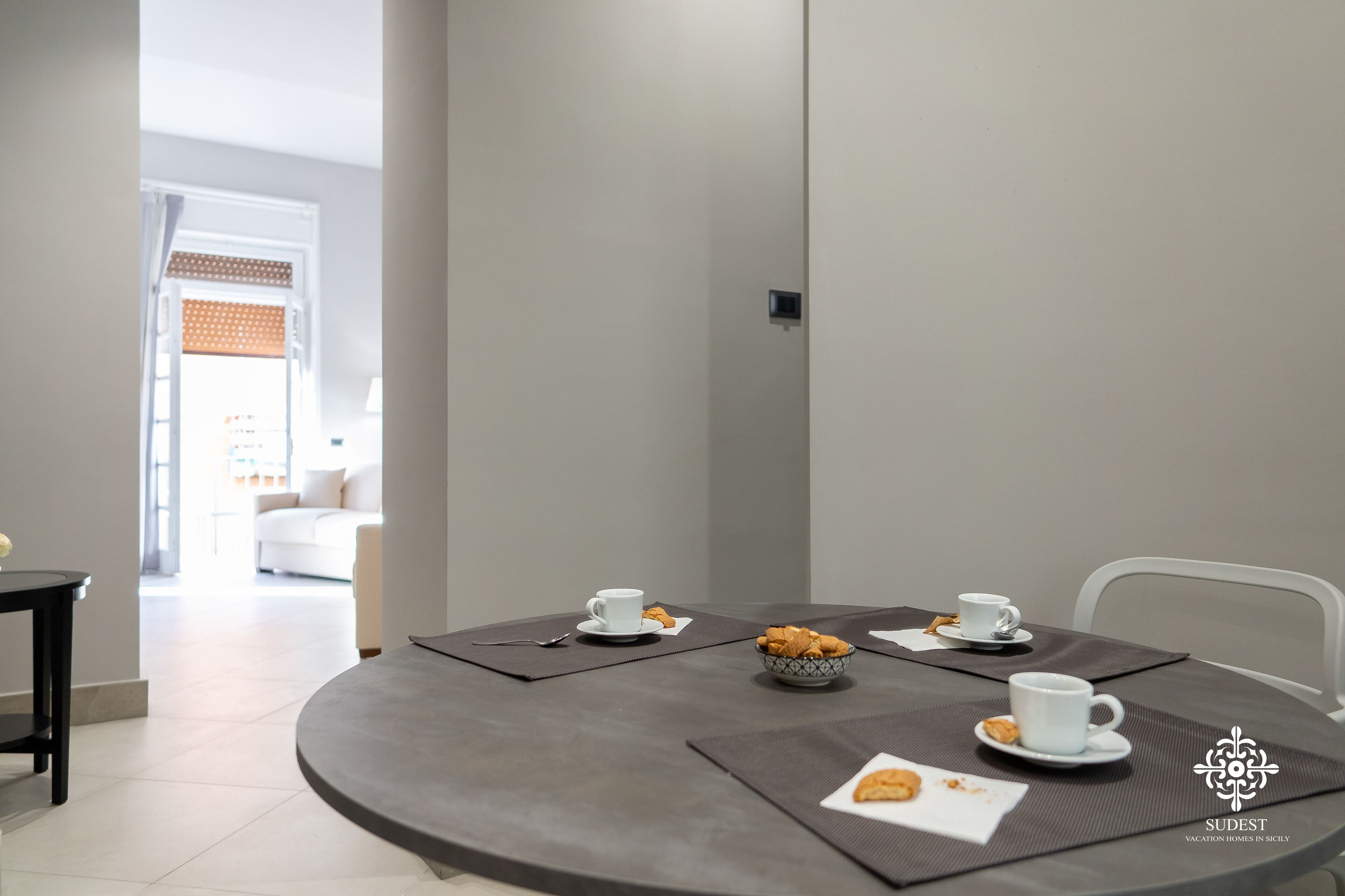 Un coin repas moderne avec une table ronde, deux tasses blanches, un bol de biscuits et une petite assiette contenant un biscuit.