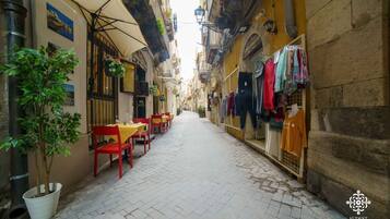 Una calle estrecha con un café a la izquierda, con mesas al aire libre y una maceta.