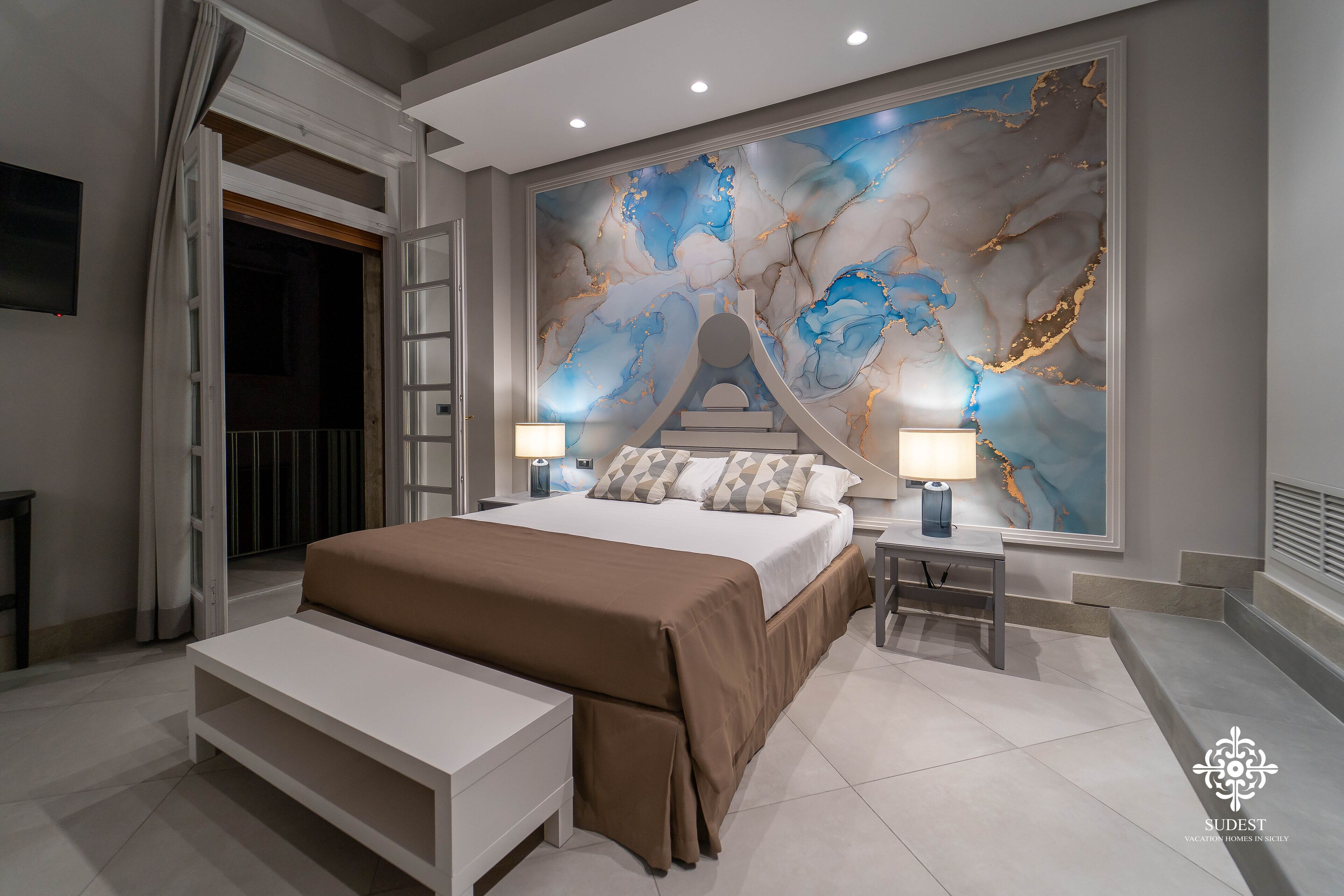 A modern bedroom with a large bed, bedside lamps, a bench, and a decorative wall mural.