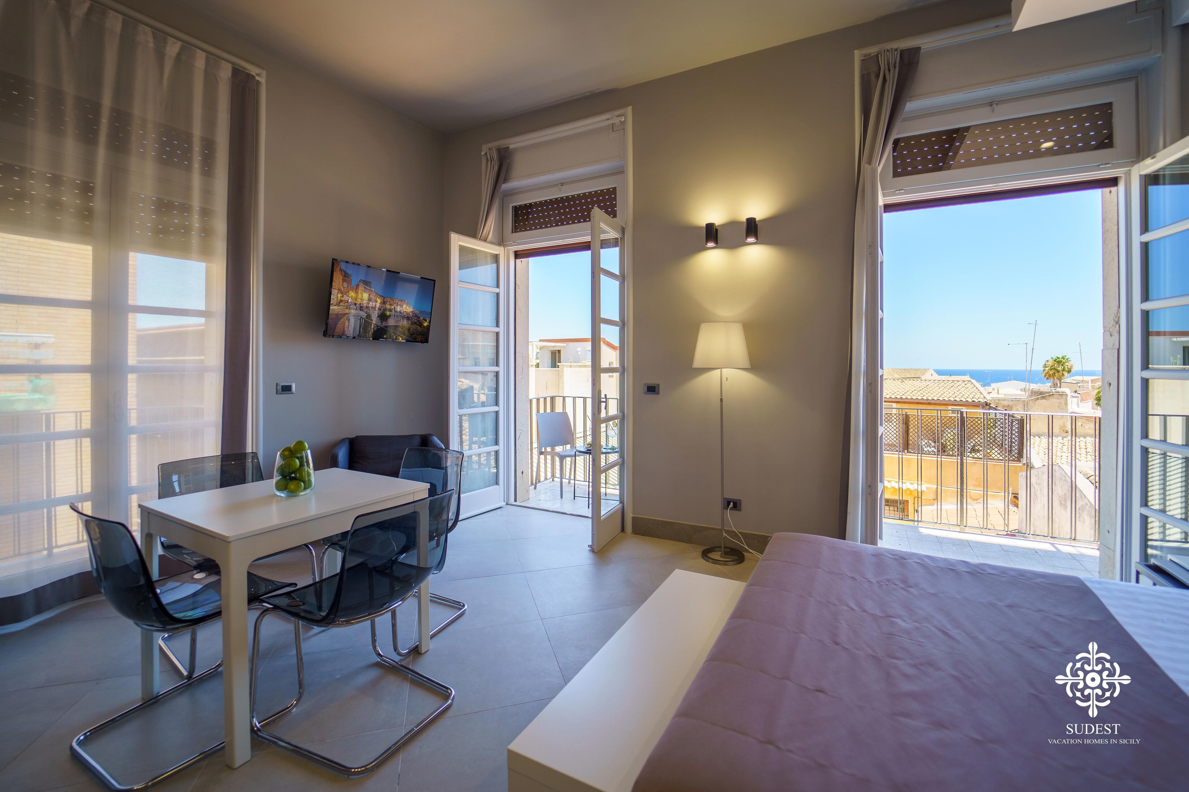 Een hotelkamer met een bed, een eettafel met stoelen, een televisie en een balkon met uitzicht op zee.