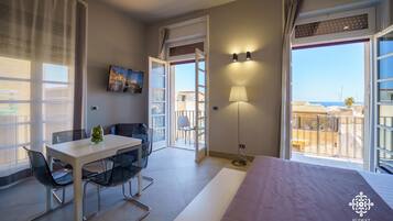 Habitación de hotel con cama, mesa de comedor con sillas, televisor y balcón con vista al mar.