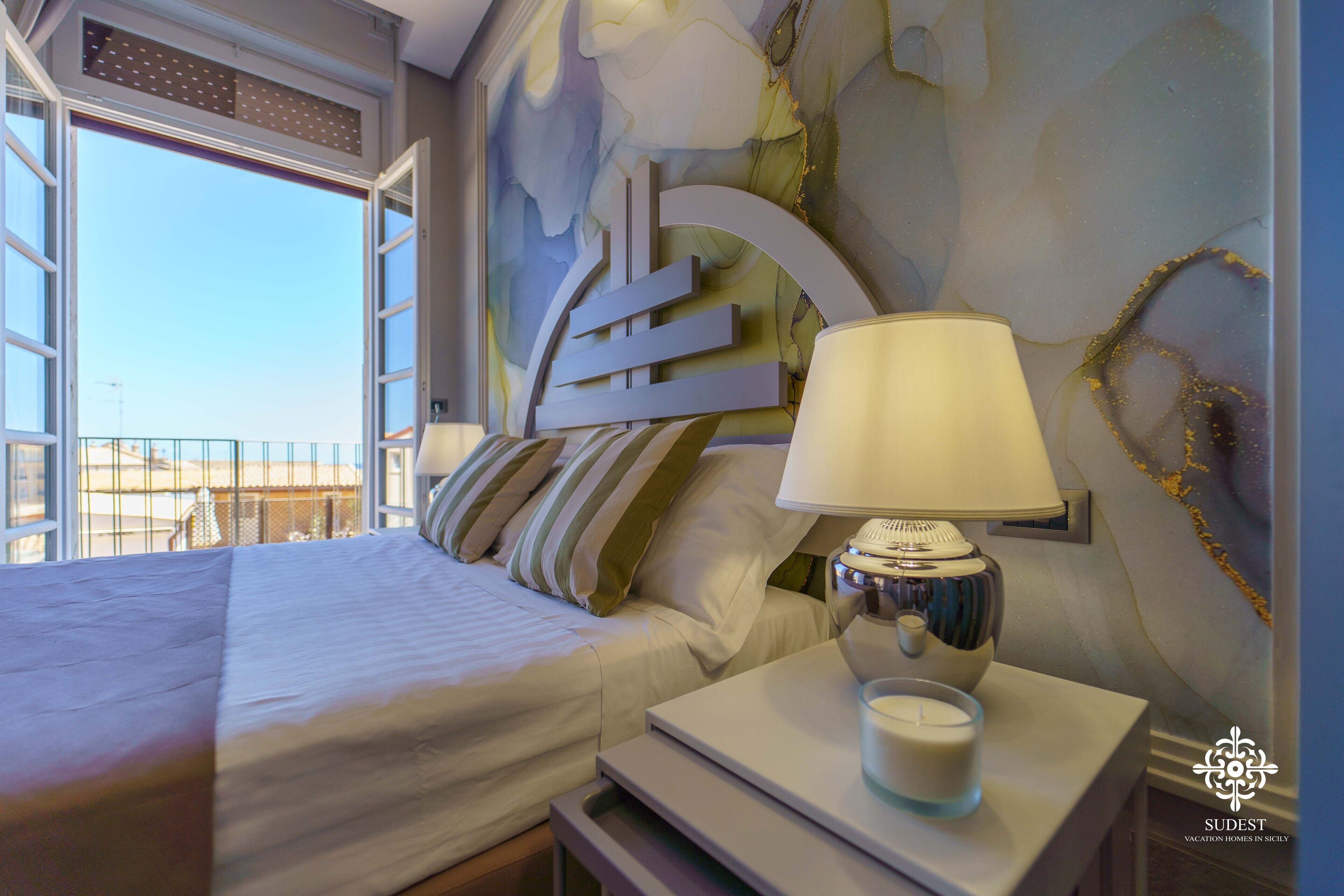 Une chambre d’hôtel avec un lit, une table de chevet avec une lampe, un mur décoratif et une vue sur l’extérieur.