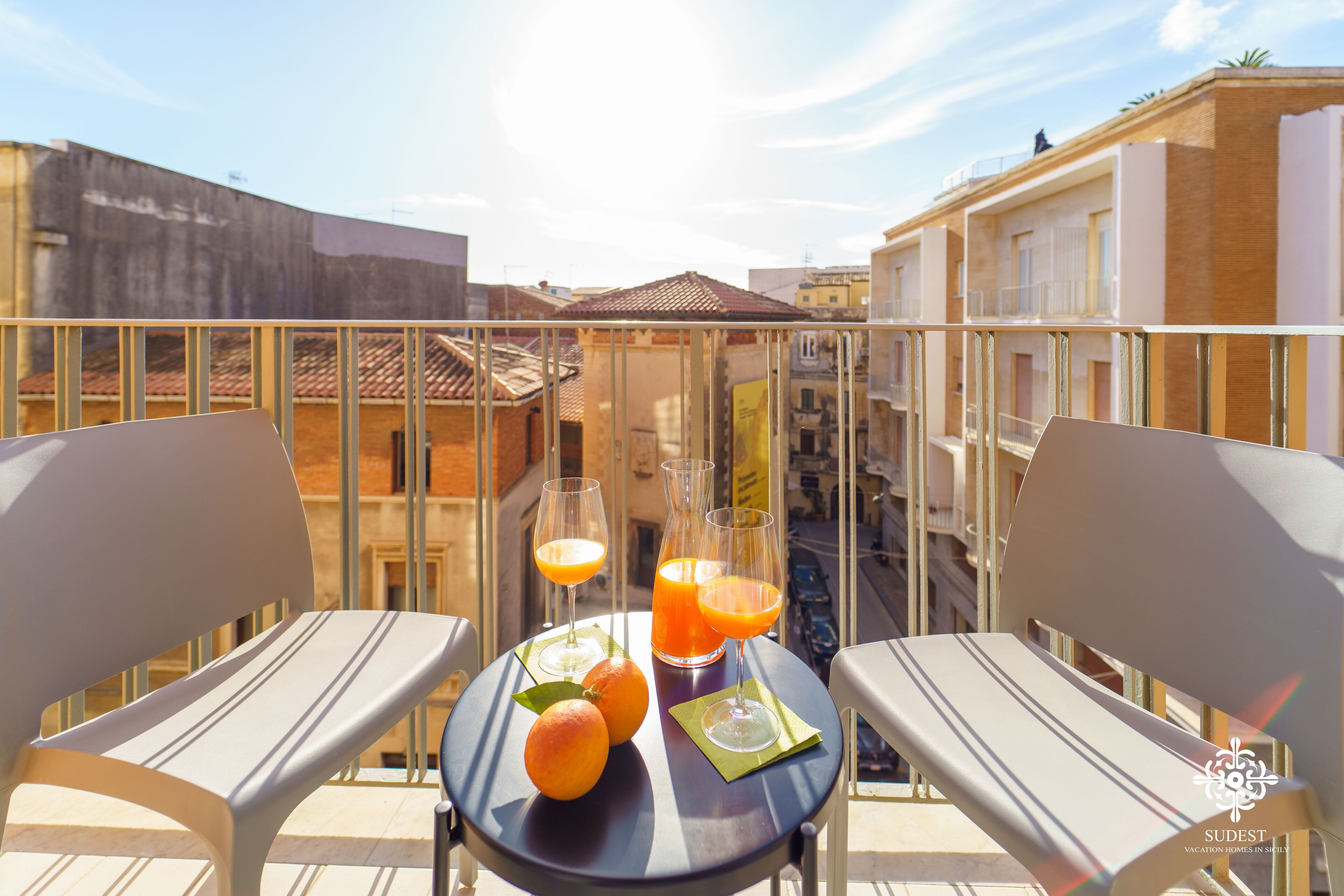Ein Balkon mit zwei Stühlen, einem Tisch und einer Orangensaftflasche.