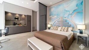 A modern hotel room with a large bed, a bench, a desk, and a kitchenette. - Matteotti Luxury Residence (Syracuse)