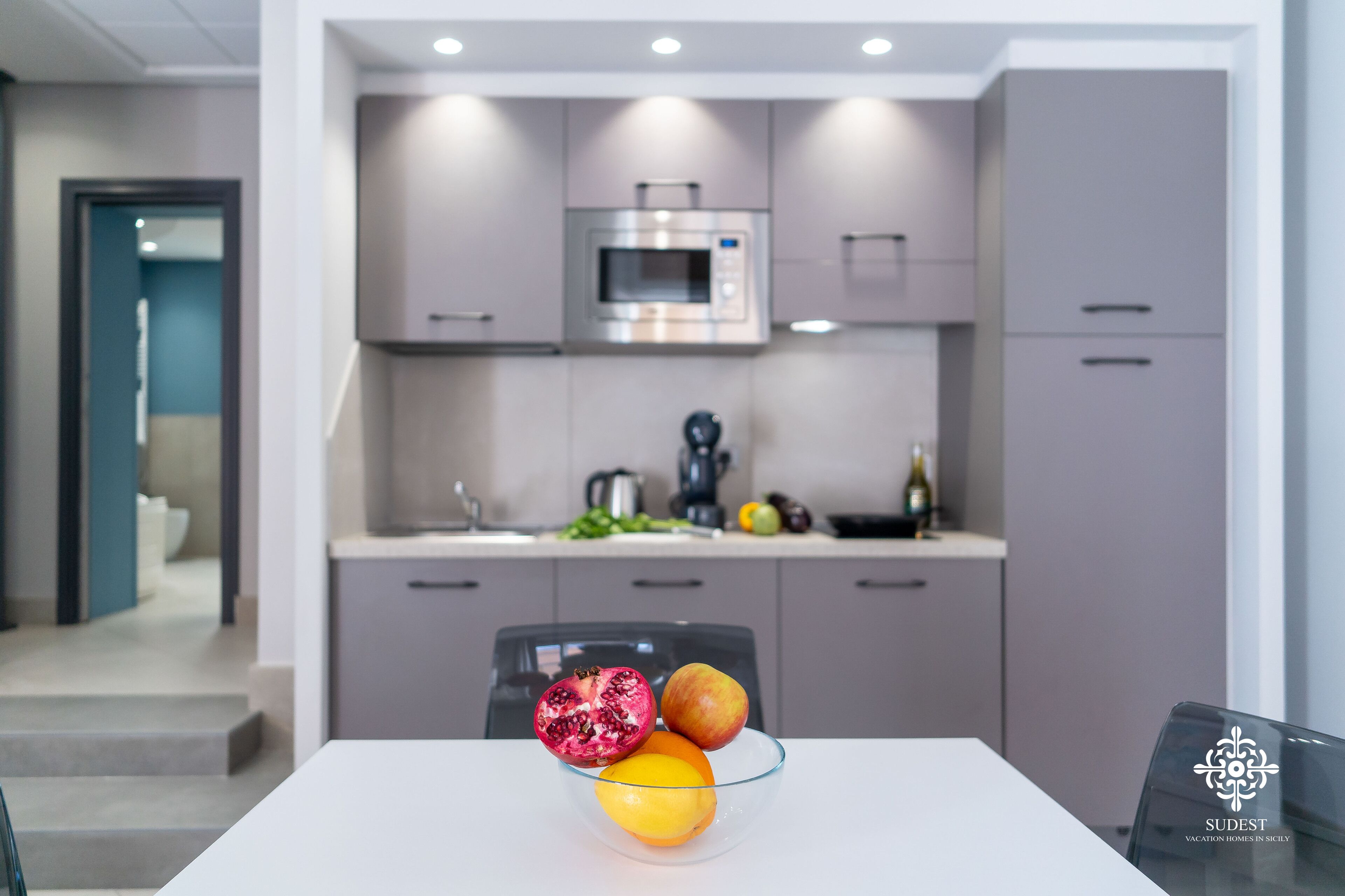 A modern kitchen with a microwave, cabinets, and a glass table with fruits.