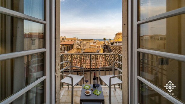 A balcony with two white chairs and a table with a bottle of wine and snacks. - Matteotti Luxury Residence (Syracuse)