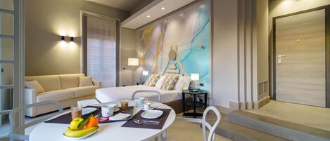 A modern hotel room with a bed, bedside tables, a dining area with a table and chairs, and a large abstract painting on the wall.
