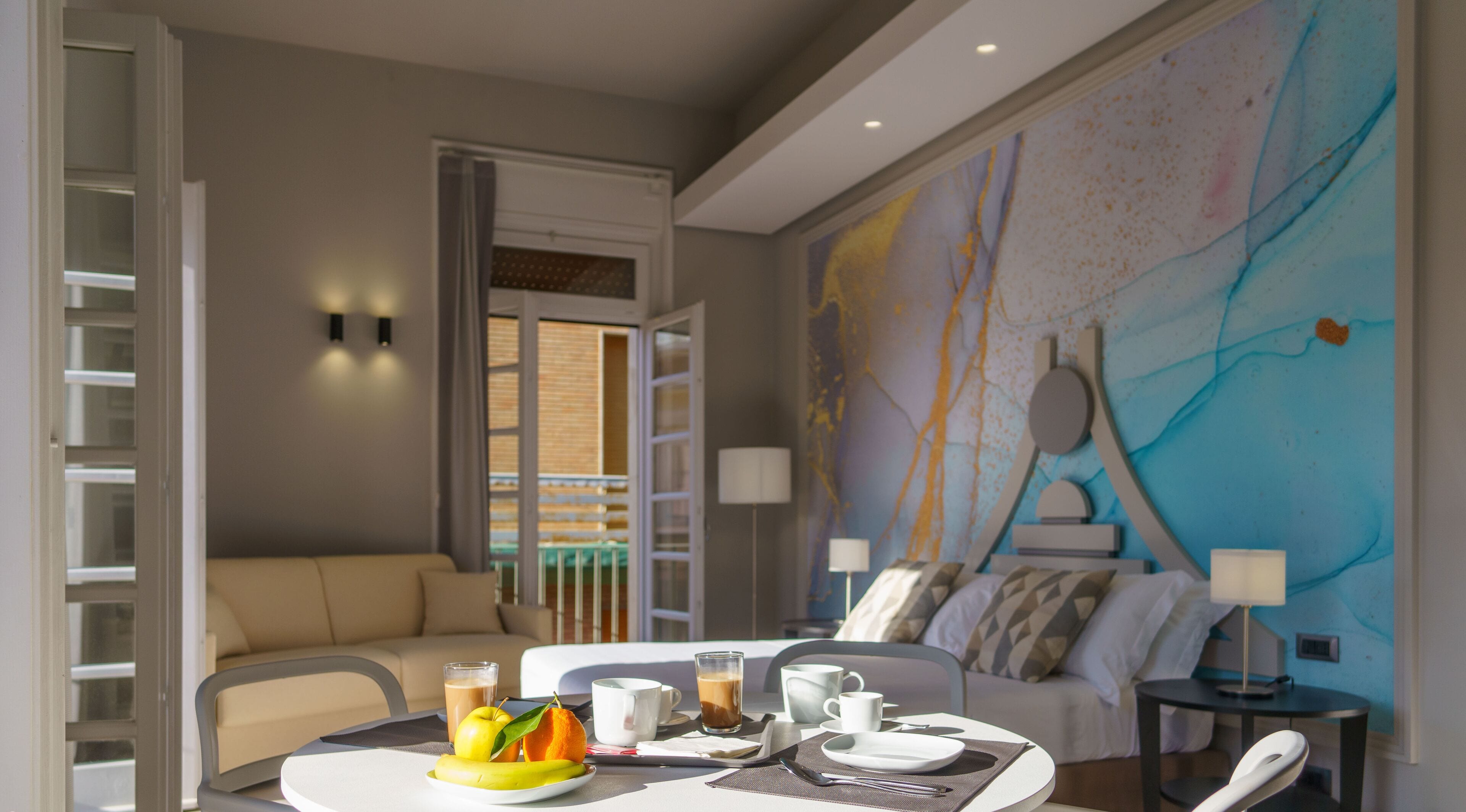 A modern hotel room with a dining area, a sofa, and a large abstract mural on the wall.