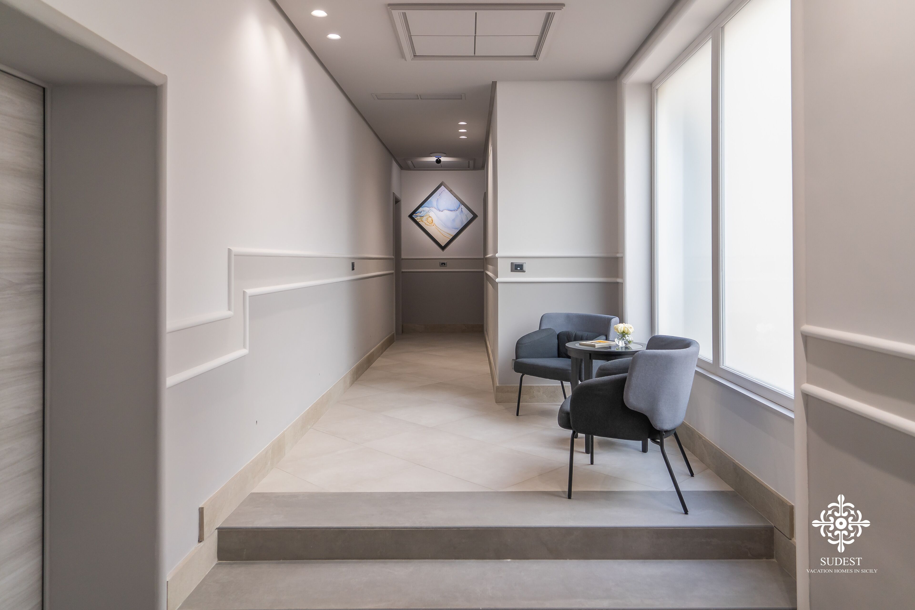 A modern hotel corridor with a staircase leading to a seating area with a table and chairs.