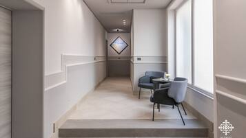 A modern hotel corridor with a staircase leading to a seating area with a table and chairs.