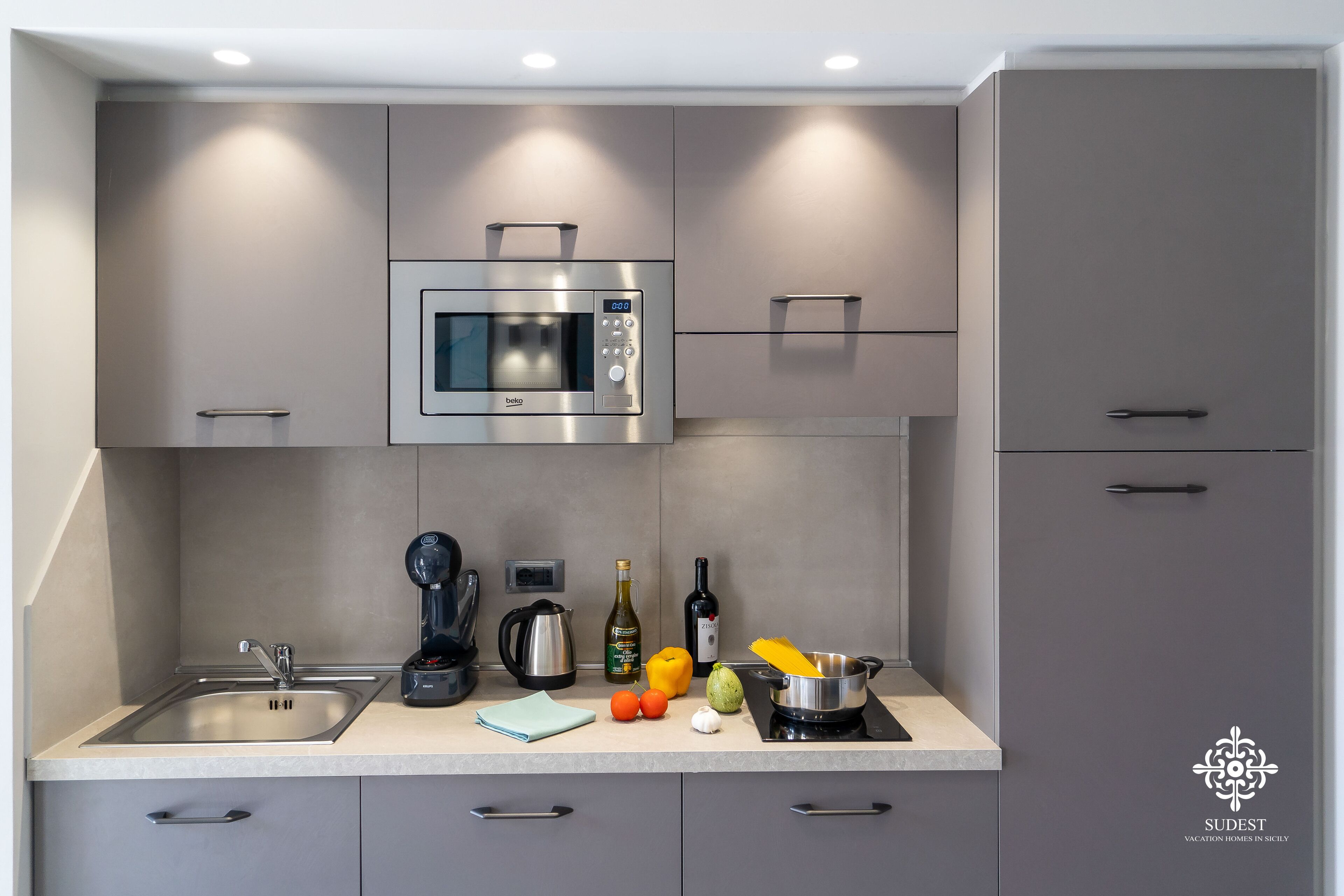 A modern kitchen with a built-in microwave, a kettle, a coffee machine, and a sink.