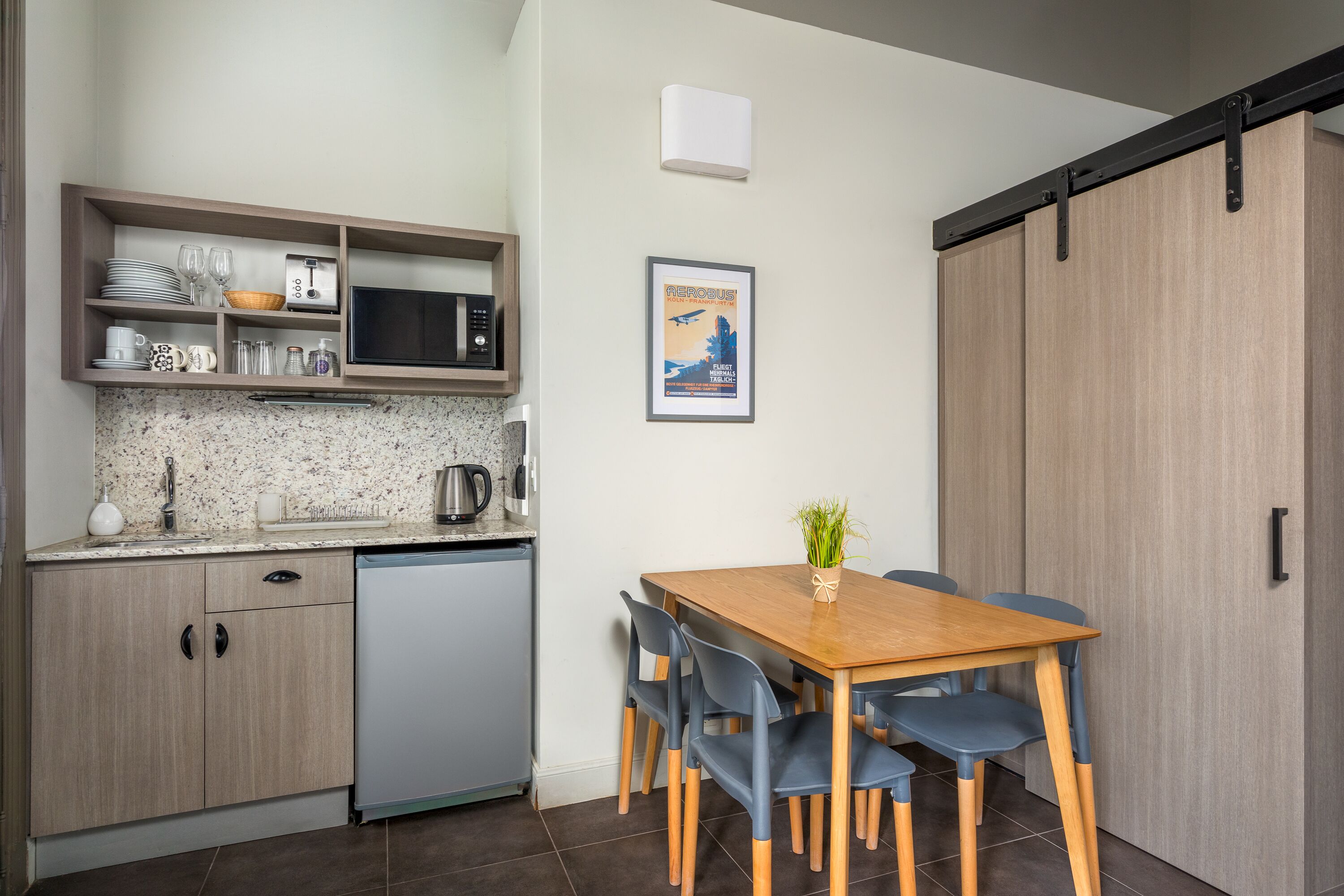 Cocina compacta con microondas, tostadora y lavamanos. Hay una mesa de comedor con sillas e imagen en el marco en la pared.