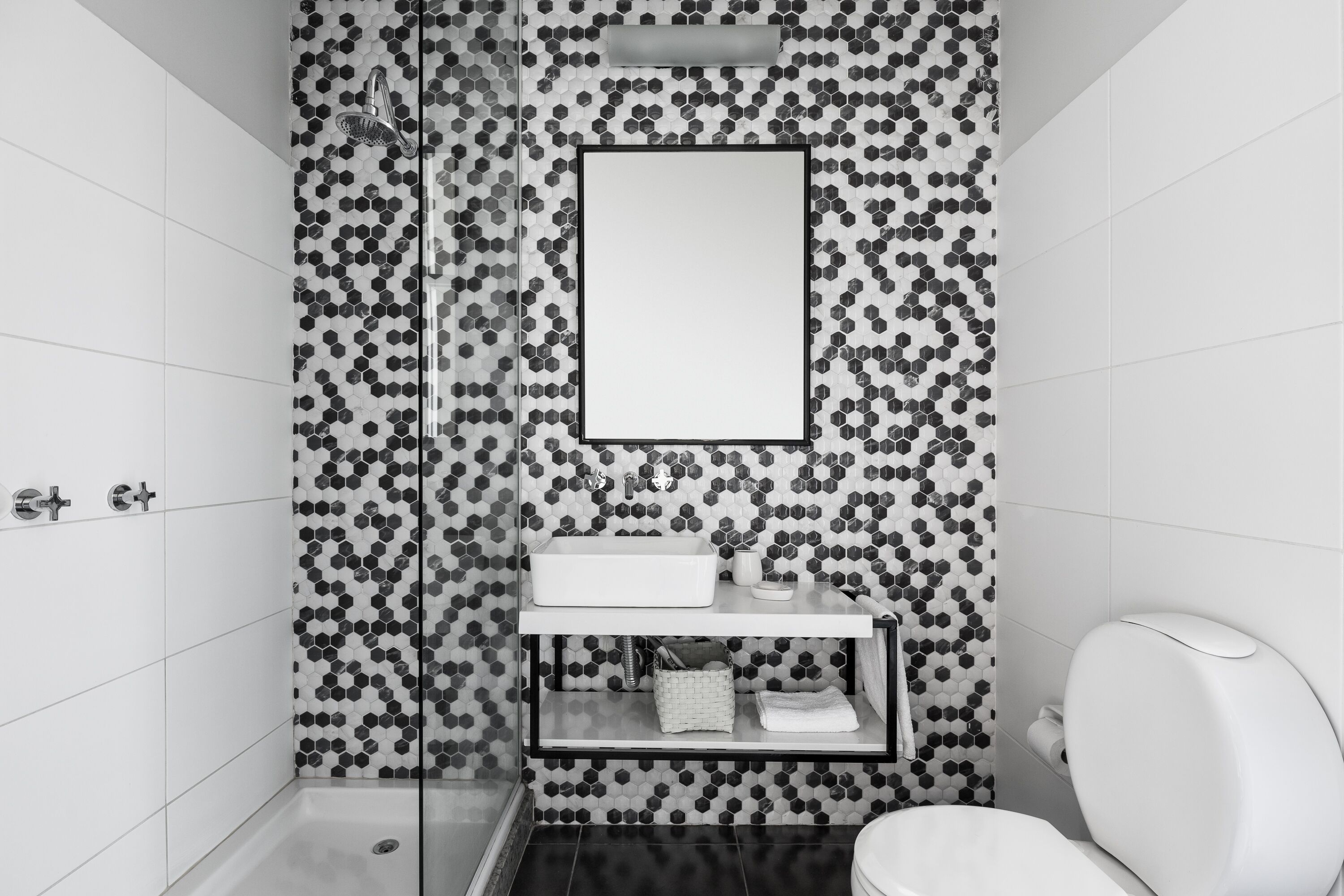 A bathroom with a hexagonal tile backsplash, a rectangular mirror, a white sink, and a toilet.
