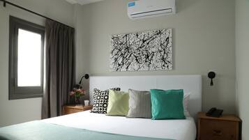 Une chambre d’hôtel avec un lit, une table de chevet, un climatiseur fixé au mur et une fenêtre avec des rideaux.