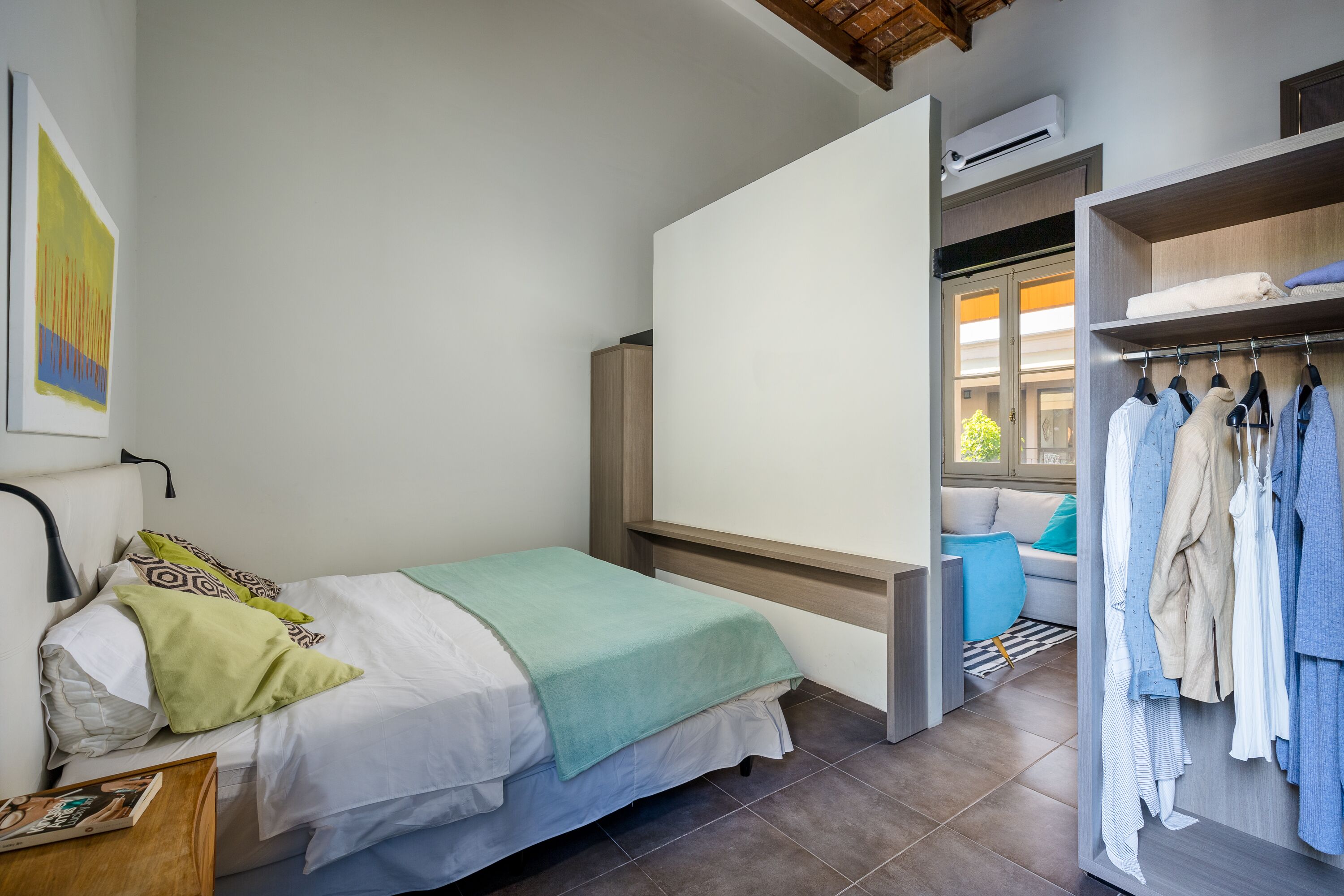 A bedroom with a bed, a wardrobe, and a view of a living area.