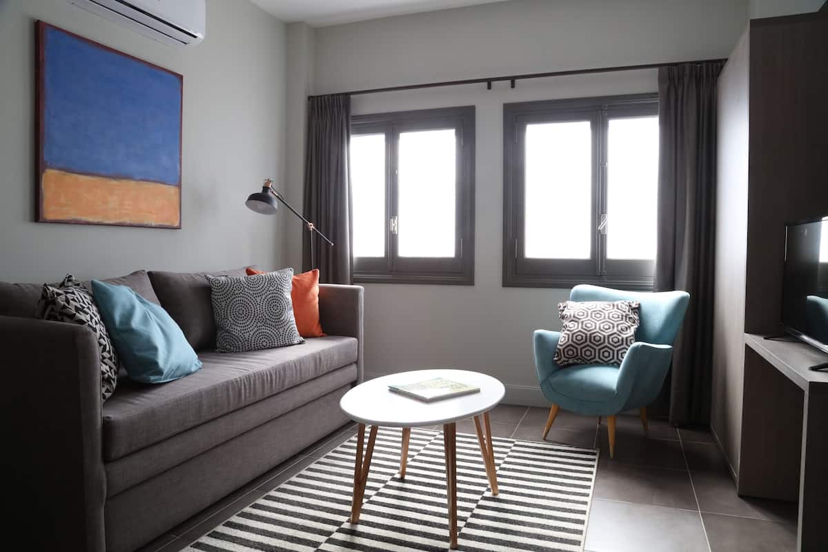A modern living room with a grey sofa, a blue armchair, a white coffee table, and a large window with curtains.
