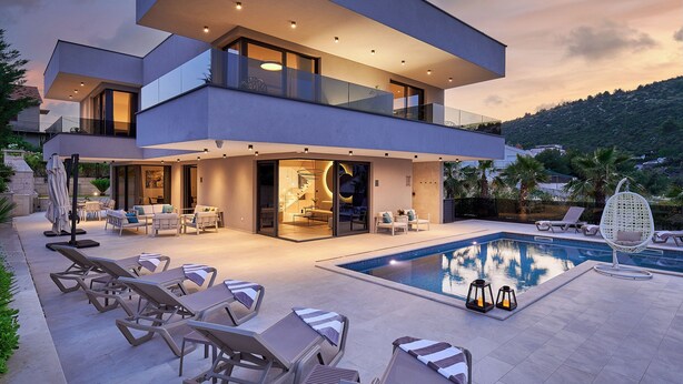 Ein modernes, zweistöckiges Haus mit Swimmingpool, Sitzgelegenheiten im Freien und einem Balkon mit Blick auf den Pool.