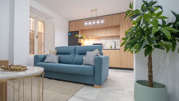A modern living room with a blue sofa, a round coffee table, and a potted plant. - Cadiz Magnolia Apartment (Cádiz)