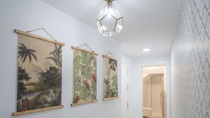 A hallway with three framed botanical prints on the wall, a geometric pendant light, and a bathroom visible through an open door. - Cadiz Magnolia Apartment (Cádiz)
