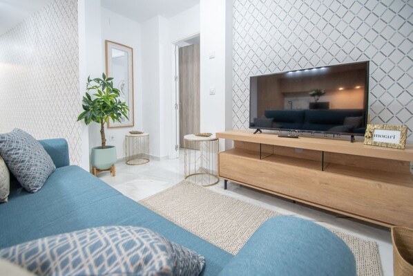 A modern living room with a blue sofa, a TV on a wooden stand, and a small plant.
