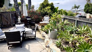 An outdoor patio with wicker furniture, a stone planter with various plants, and a view of neighboring houses. - South Laguna Beach summer rental near Montage Resort (Laguna Beach)