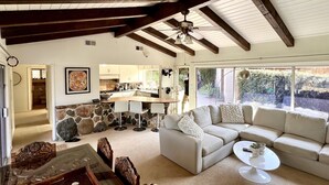 A spacious living area with a large sofa, a coffee table, and a stone accent wall. A kitchen is visible in the background, and there is a large window providing natural light. - South Laguna Beach summer rental near Montage Resort (Laguna Beach)