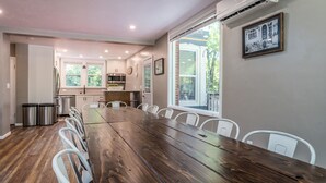 A spacious dining area with a long wooden table, white chairs, and a kitchen in the background. - Group Retreat | Hot Tub, Arcades, Private Trails (Ephraim)