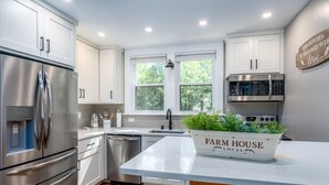 A modern kitchen with stainless steel appliances, white cabinetry, and a farmhouse sign on the counter. - Group Retreat | Hot Tub, Arcades, Private Trails (Ephraim)