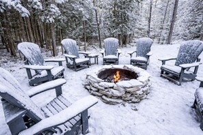 A snow-covered outdoor seating area with Adirondack chairs arranged around a stone fire pit. - Group Retreat | Hot Tub, Arcades, Private Trails (Ephraim)