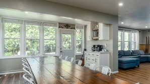 A spacious kitchen with a long wooden table, white cabinets, and large windows offering a view of the outdoors. - Group Retreat | Hot Tub, Arcades, Private Trails (Ephraim)