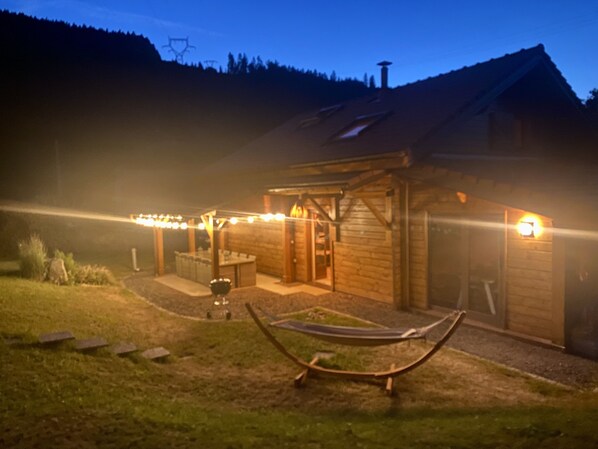 A wooden cabin with a porch, a hammock, and string lights.