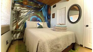 A bedroom with a bed, a peacock pillow, a mirror, and a colorful tapestry on the wall. - Relax with spectacular views @ Bear Dance Cabin (Running Springs)